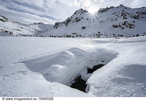 Sun shines over snow-covered mountain peaks  gorge peaks and heads of the Tarn Valley  open snow cover in front with a flowing brook underneath  Wattentaler Lizum  Tuxer Alps  Tyrol  Austria  Europe