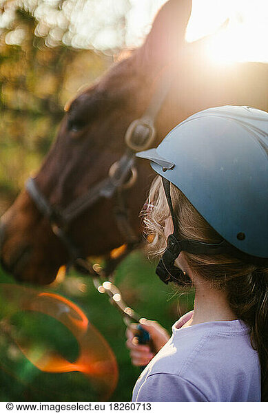 Sunflare with girl in riding helmet leading horse outside in fall