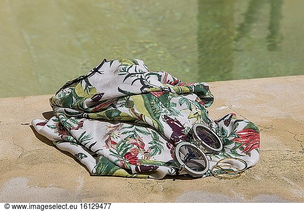 Sunglasses and tropical dress on the edge of a swimming pool. Summer concept with copy space.