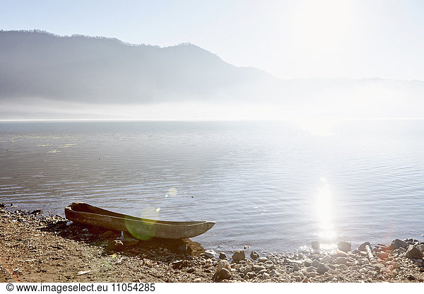 Sunlight on the water of a mountain lake  and a dug out canoe on the shore.
