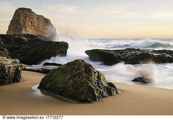 Sunset along the central California coast with waves crashing onto the large rocks on the beach; Santa Cruz  California  United States of America