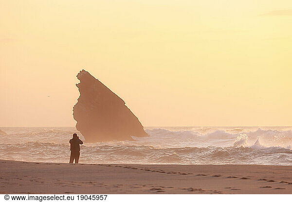 Sunset at rocky coastline of Adraga beach with man silhouette