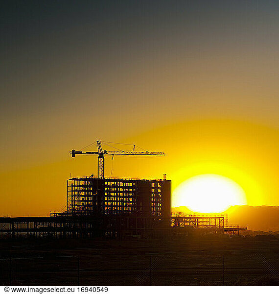 Sunset behind high rise building construction site and cranes.
