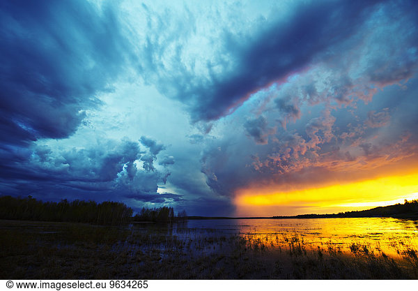 Sunset on the horizon over a lake  and storm clouds rising.