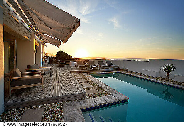 Sunset over ocean behind modern  luxury patio swimming pool