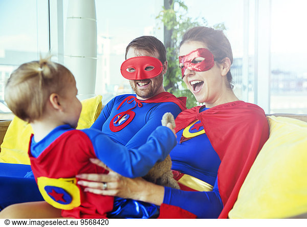 Superhero parents playing with daughter on living room sofa