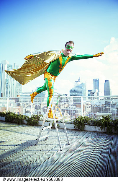 Superhero posing on stepladder on city rooftop