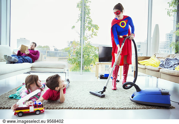 Superhero vacuuming around family in living room