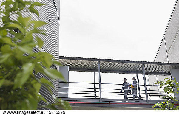Supervisors walking on elevated walkway between factory buildings