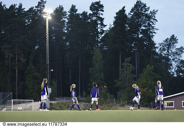 Surface level view of girls practicing soccer on field against trees