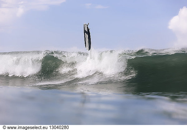 Surfboard over splashing wave in sea against sky