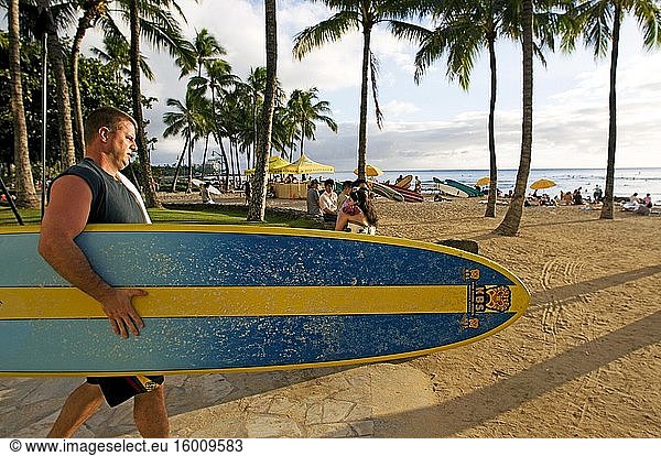 Surfer am berühmten Waikiki Beach. Kalakaua Avenue. O'ahu. Hawaii. Das weltberühmte Viertel Waikiki liegt an der Südküste von Honolulu und war einst ein Spielplatz für die hawaiianischen Könige. Waikiki  auf Hawaii als sprudelnde Gewässer bekannt  wurde der Welt vorgestellt  als 1901 das erste Hotel  das Moana Surfrider  an seinen Ufern gebaut wurde. Heute ist Waikiki das wichtigste Hotel- und Feriengebiet Oahus und ein pulsierender Treffpunkt für Besucher aus aller Welt. Entlang des Hauptstreifens der Kalakaua Avenue finden Sie erstklassige Einkaufsmöglichkeiten  Restaurants  Unterhaltungsangebote  Aktivitäten und Resorts. Waikiki ist vor allem für seine Strände bekannt  und jedes Zimmer ist nur zwei oder drei Blocks vom Meer entfernt. Mit Leahi (Diamond Head) als Kulisse sind die ruhigen Gewässer von Waikiki wie geschaffen für eine Surfstunde. Der legendäre hawaiianische Wassersportler Duke Kahanamoku wuchs mit dem Surfen in den Wellen von Waikiki auf. Dieser olympische Goldmedaillengewinner im Schwimmen brachte den Besuchern um die Jahrhundertwende das Surfen bei und wurde später als ? Der Vater des modernen Surfens. Heute führen die Waikiki Beach Boys das Vermächtnis von Duke fort  indem sie Besuchern das Surfen und Kanufahren beibringen  und die Duke Kahanamoku-Statue ist zu einem Wahrzeichen von Waikiki geworden.