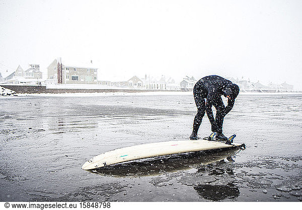 Surfer kontrolliert während eines Schneesturms in Maine die Unterseite des Brettes