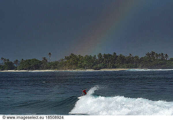 Surfer on a wave under a rainbow