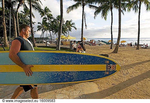 Surfer on the famous Waikiki Beach. Kalakaua Avenue. O'ahu. Hawaii. Located on the south shore of Honolulu  the world-famous neighborhood of Waikiki was once a playground for Hawaiian royalty. Known in Hawaiian as 'spouting waters ' Waikiki was introduced to the world when its first hotel  the Moana Surfrider  was built on its shores in 1901. Today  Waikiki is Oahu?.s main hotel and resort area and a vibrant gathering place for visitors from around the world. Along the main strip of Kalakaua Avenue you'll find world-class shopping  dining  entertainment  activities and resorts. Waikiki is most famous for its beaches and every room is just two or three blocks away from the sea. With Leahi (Diamond Head) as your backdrop  the calm waters of Waikiki are perfect for a surfing lesson. In fact  legendary Hawaiian waterman Duke Kahanamoku grew up surfing the waves of Waikiki. This Olympic gold medalist in swimming actually taught visitors how to surf at the turn of the century and was later known as ?. ?The father of modern surfing. ?.Today  the Waikiki Beach Boys perpetuate Duke?.s legacy by teaching visitors how to surf and canoe and the Duke Kahanamoku Statue has become an iconic symbol of Waikiki.