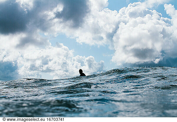 Surfer sitzt allein unter einem stimmungsvollen Himmel im Meer