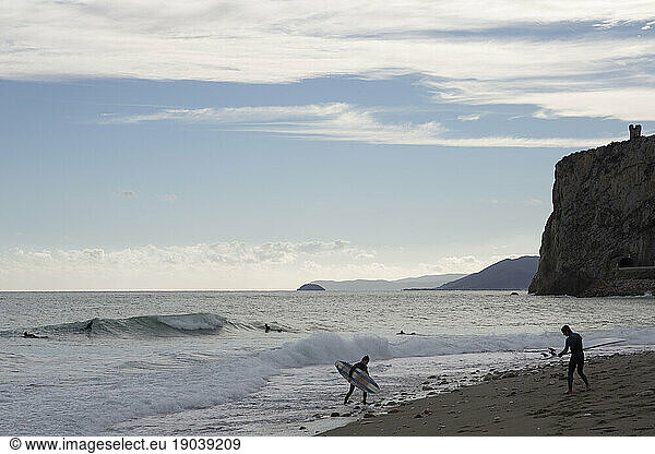 Surfers on beach and waves  Medieval tower on hill behind