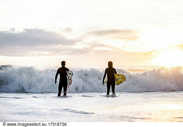 surfing boys entering the water at sunrise  background waves