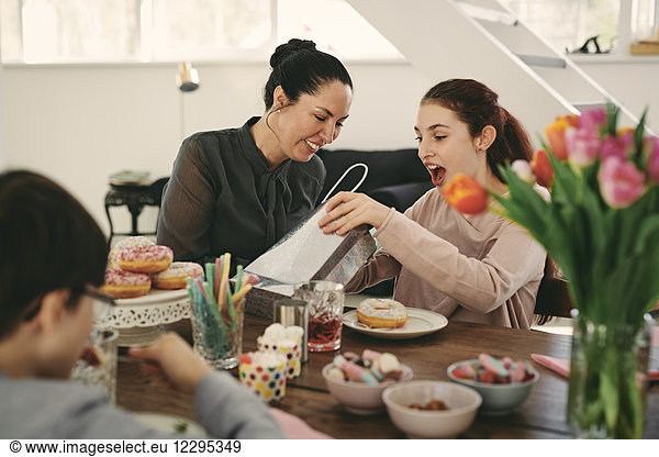 Surprised girl looking at bag while sitting with mother during meal in birthday party