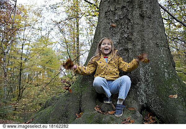 Surprised girl playing with leaves sitting on tree trunk in forest