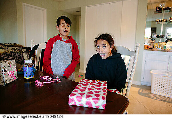 Surprised girl sits at table opening birthday presents