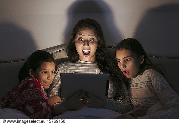 Surprised mother and daughters watching movie on digital tablet in dark bedroom
