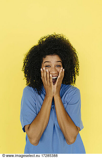 Surprised woman covering mouth with hands on yellow background