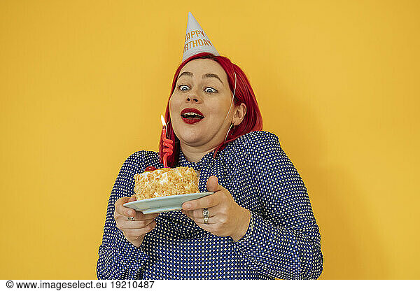 Surprised woman holding birthday cake against yellow background