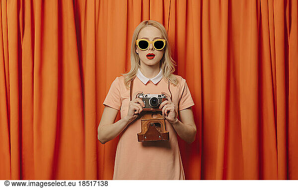 Surprised woman holding camera in front of orange curtains