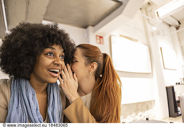 Surprised woman listening to friend whispering in her ear