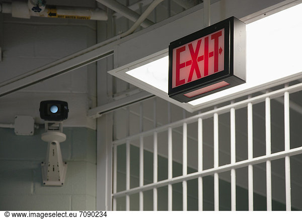 Surveillance camera  Exit sign and a barred gate at a Correctional Facility.