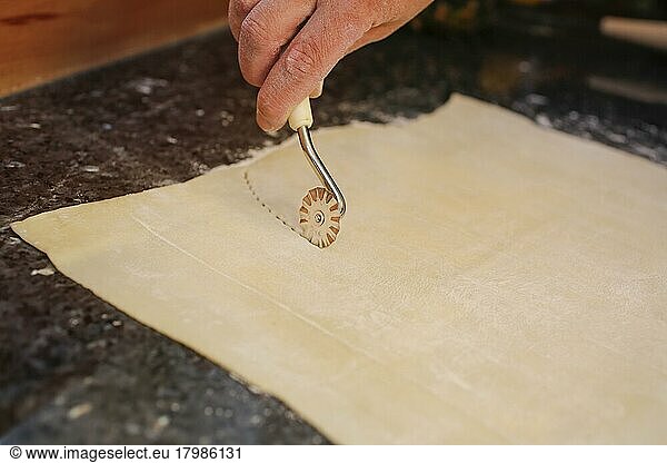Swabian cuisine  preparation of Reutlinger Schiedwecken  cutting out puff pastry with pastry wheel  man's hand  puff pastry with veal filling  hearty pie  baking  traditional Swabian dish  studio shot  food photography  Germany  Europe
