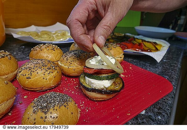 Swabian cuisine  preparation steam noodle burger  hearty  salty  yeast pastry topped with vegetables  fried zucchini slice  onion ring  yeast yeast dough  vegetarian  bake  out of the oven  typical Swabian reinterpreted  party pastry  finger food  cutting board  man's hand  traditional cuisine  food photography  studio  Germany  Europe