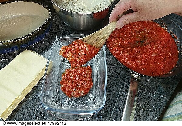 Swabian cuisine  preparing alblinsen casserole  filling tomato sauce into casserole dish  baking dish  pasta dough  pasta flat  lasagne  traditional cuisine  hearty oven dish  main dish  man's hand  spatula  studio  food photography  Germany  Europe