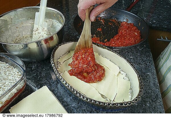 Swabian cuisine  preparing alblinsen casserole  filling tomato sauce into casserole dish  pasta dough  pasta patties  lasagne  baking dish  traditional cuisine  hearty oven dish  main dish  man's hand  spatula  studio  food photography  Germany  Europe