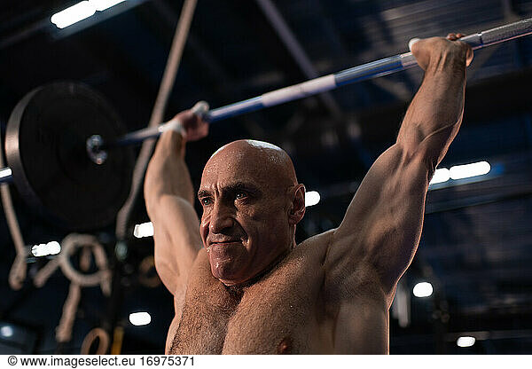 Sweaty elderly sportsman lifting barbell