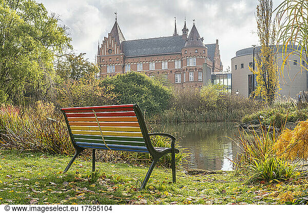 Sweden  Skane County  Malmo  Rainbow colored bench standing in front of park pond with Malmo City Library in background