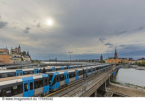Sweden  Stockholm County  Stockholm  Sun shining over subway trains passingÂ Sodra Jarnvagsbron bridgeÂ during cloudy weather