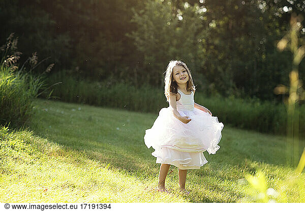 Sweet little girl in white dress twirling and dancing in a meadow.