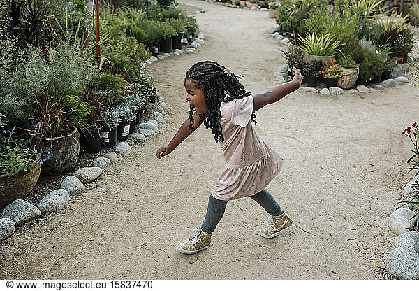 Sweet young black girl with long braids dancing on garden path