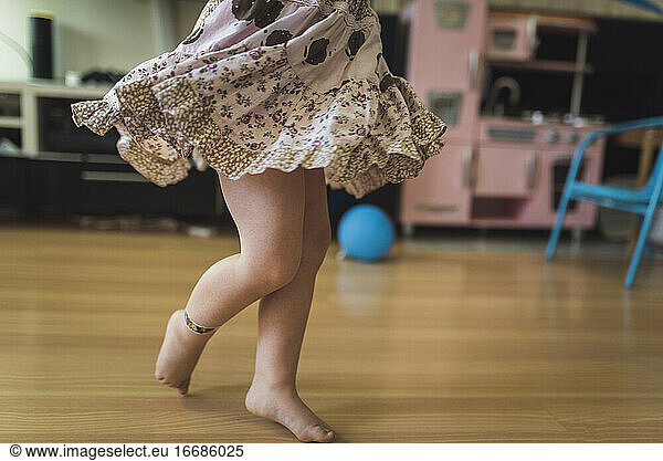Swirling skirt of bare-legged 4 yr old girl dancing in playroom