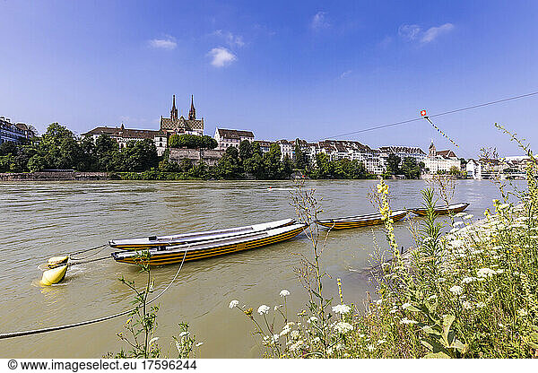 Switzerland  Basel-Stadt  Basel  Rowboats moored on bank of Rhine river in summer with city buildings in background