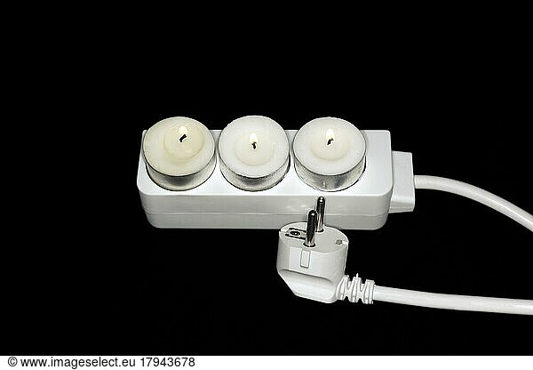 Symbolic photo for blackout or power saving  three tea lights stuck in a triple socket  studio photography with black background