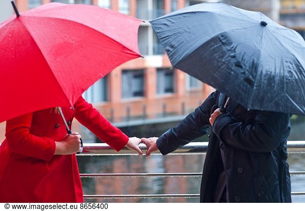 Symmetrical couple holding handrail and carrying umbrella's