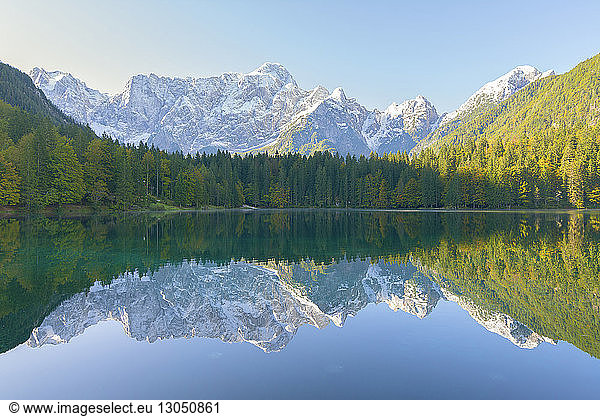 Symmetry view of lake by trees against mountain ranges during winter