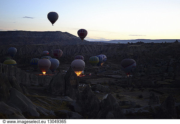 Szenische Ansicht von Heißluftballons  die bei Sonnenuntergang über die Landschaft gegen den Himmel fliegen