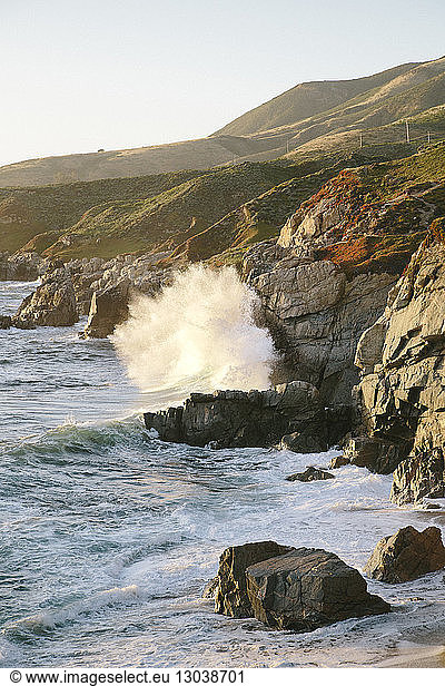 Szenische Ansicht von Wellen  die sich an Felsen gegen den klaren Himmel brechen