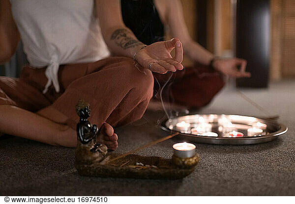 Tätowierte Frau meditiert neben Weihrauch und Kerzen