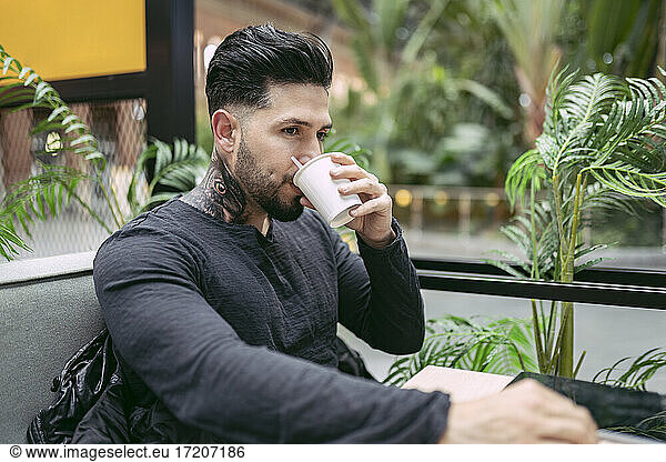 Tätowierter Hipster-Mann trinkt Kaffee im Laden