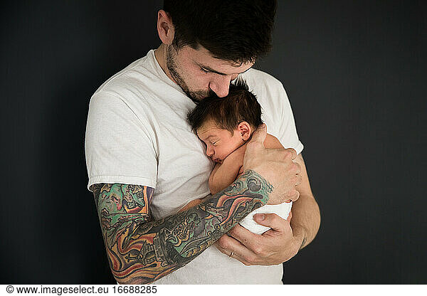 Tätowierter Millennial-Vater küsst neugeborenen Sohn  der eine Windel trägt